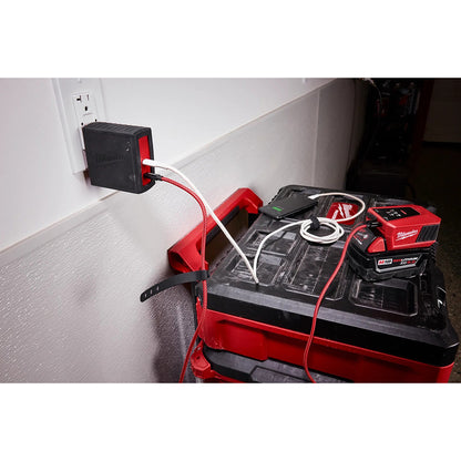 Milwaukee tool battery pack charging on a toolbox with a power outlet in the background.