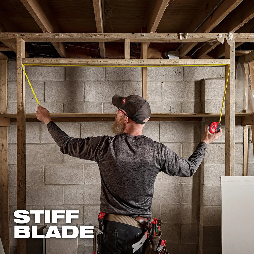 Man measuring wall studs with a tape measure in a construction setting, with 'Stiff Blade' branding.