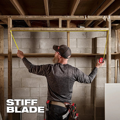 Man measuring wall studs with a tape measure in a construction setting, with 'Stiff Blade' branding.