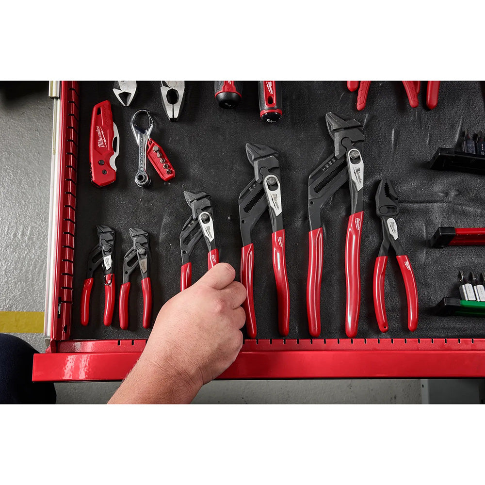 Hand reaching into a tool drawer filled with red pliers and other tools.