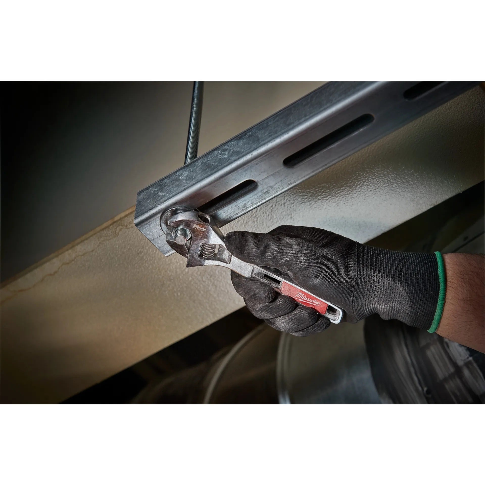 Hand using a wrench on a metal component, likely part of a vehicle's suspension system.