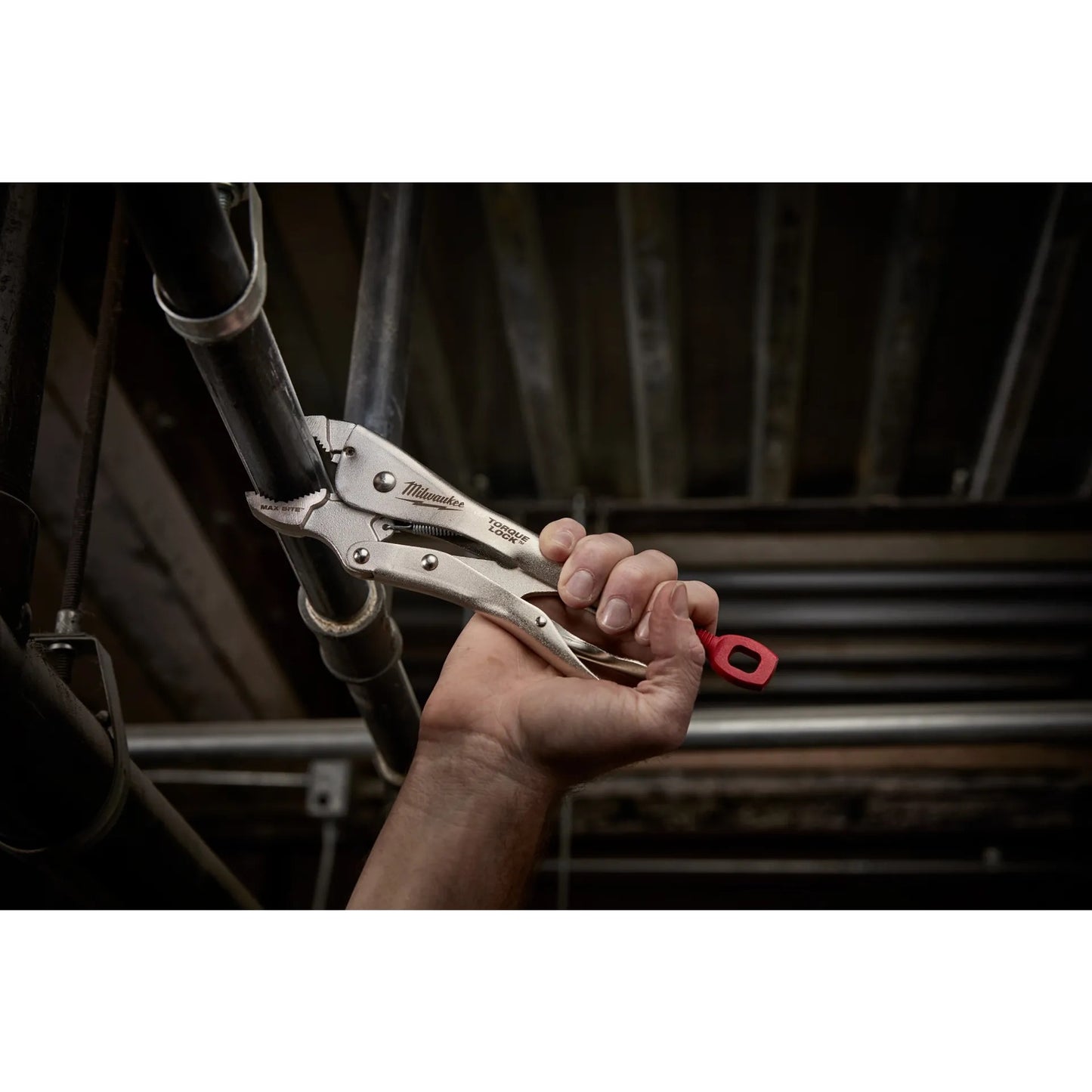 Hand holding a pair of locking pliers with a red handle in a workshop setting