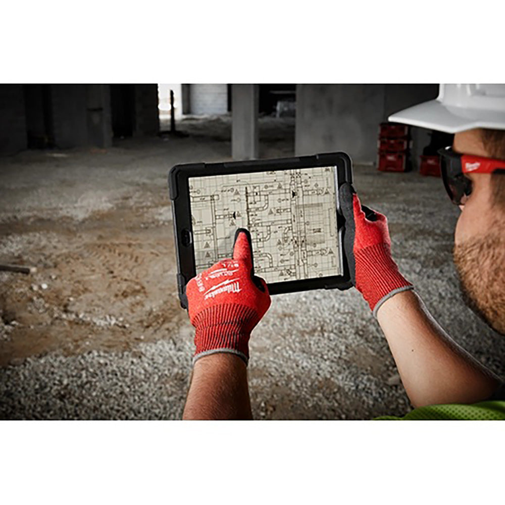 Person wearing red gloves holding a tablet with architectural plans on a construction site.