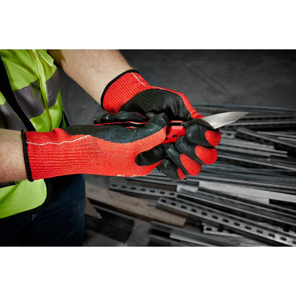 Person wearing red and black gloves holding a knife in a workshop setting.
