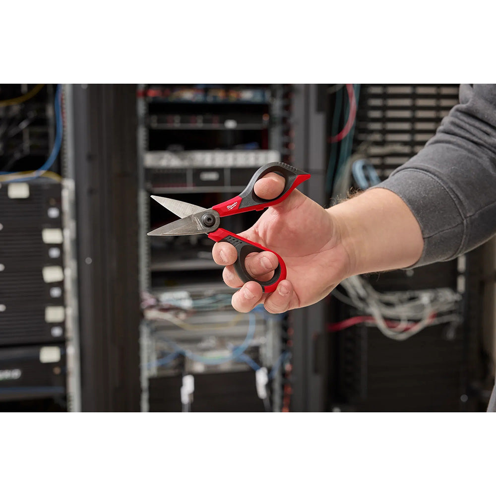 Hand holding red and black scissors in front of a server rack.