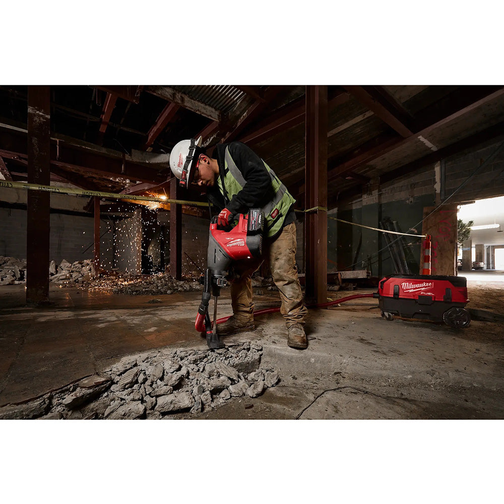 Worker using a Milwaukee tool in a construction setting with debris and equipment.