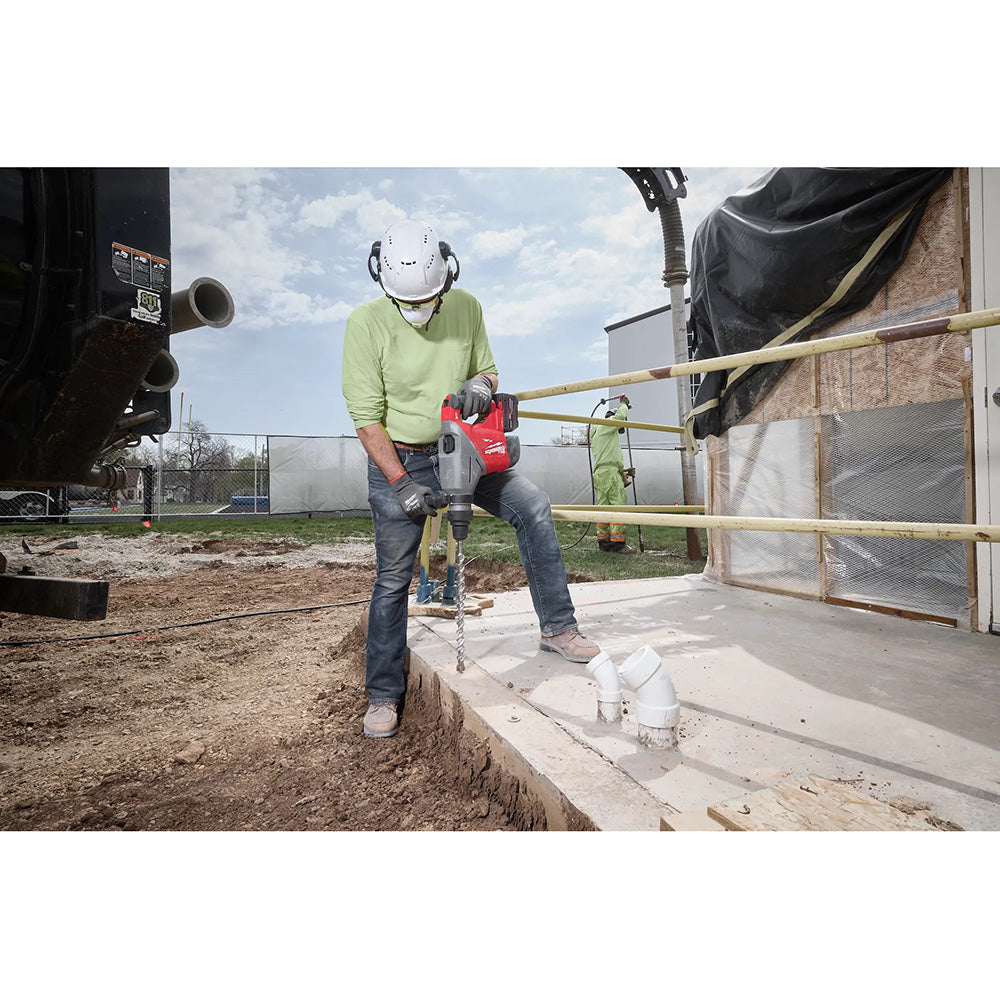 Person using a drill on a construction site with a building in the background