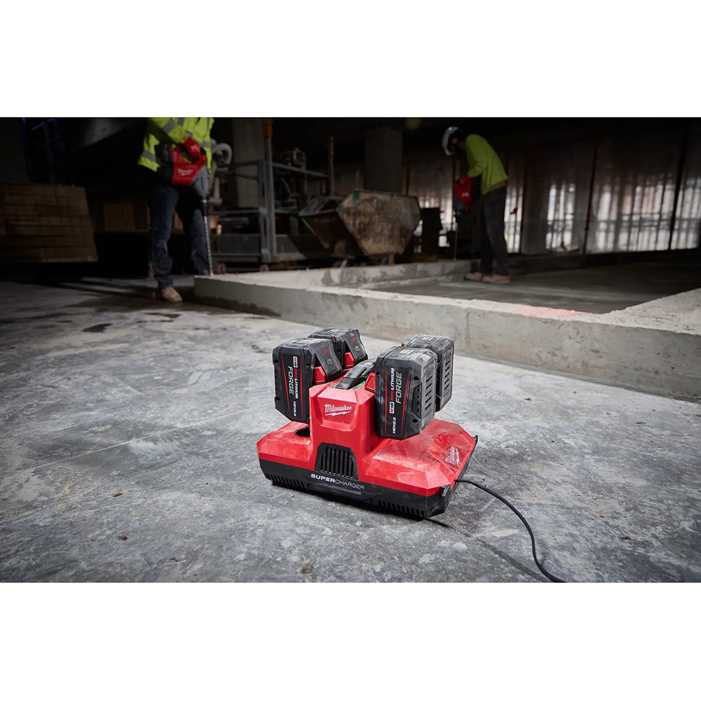 Red SuperCharger with batteries on a concrete floor, with workers in the background.