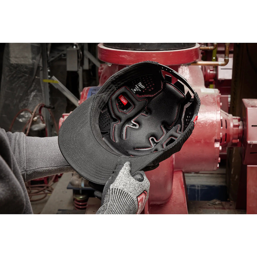 Person wearing a black cap with a red logo in front of a large industrial machine.